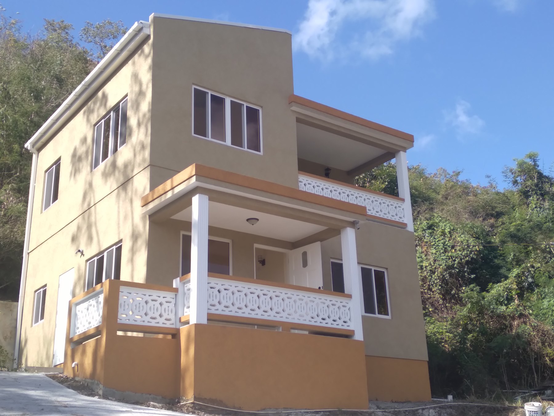 Two-storey beige home beside a green hillside